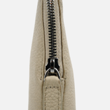 Close-up of a light beige pebbled leather clutch or wristlet with a black metal zipper, shown against a plain light gray background.