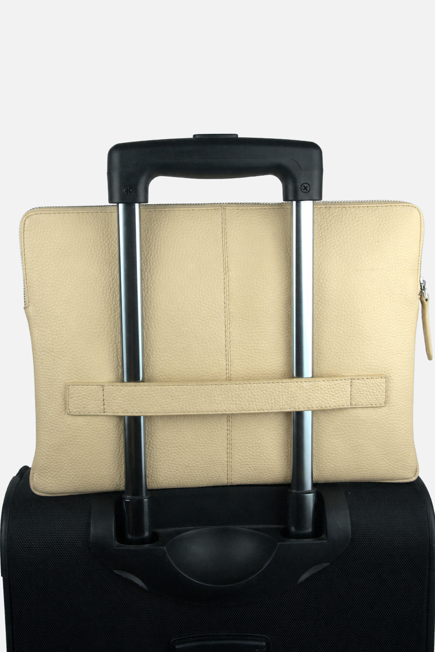 A beige leather laptop sleeve with a horizontal strap closure, shown from the back and strapped onto the handle of a black rolling suitcase against a plain white background.