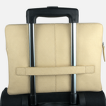 A beige leather laptop sleeve with a horizontal strap closure, shown from the back and strapped onto the handle of a black rolling suitcase against a plain white background.