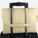 A beige leather laptop sleeve with a horizontal strap closure, shown from the back and strapped onto the handle of a black rolling suitcase against a plain white background.